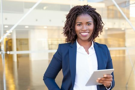 Businesswoman holding tablet pc and smiling at camera. Cheerful young African American businesswoman holding digital tablet and looking at camera. Wireless technology concept